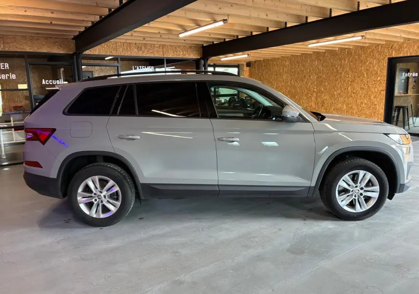 Vue latérale droite d'un Skoda Kodiaq gris clair 2023, SUV 7 places avec jantes alliage et vitres teintées, en intérieur.