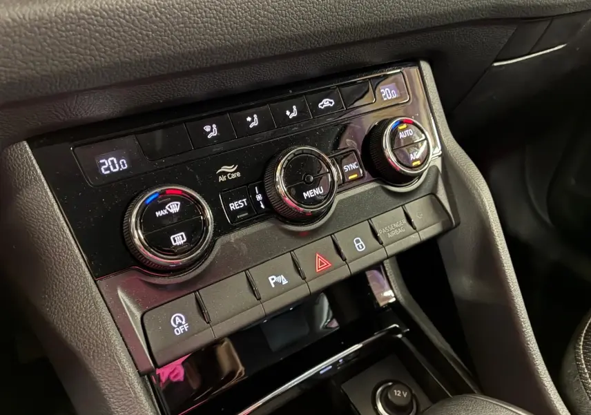 Vue rapprochée du tableau de bord central du Skoda Kodiaq gris clair 2023, mettant en valeur les commandes de climatisation et les boutons de sécurité.