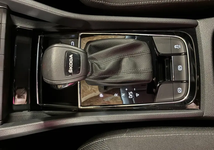 Gros plan sur la console centrale avec levier de vitesse automatique noir marqué SKODA, entouré de boutons de contrôle.
