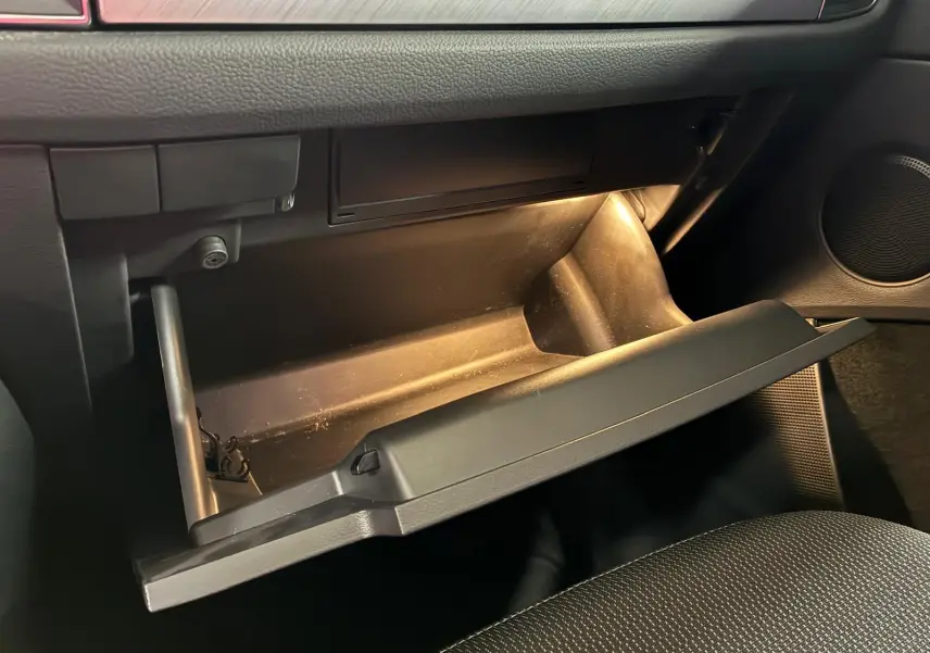 Vue intérieure du coffre à gants ouvert du Skoda Kodiaq gris clair 2023, mettant en valeur l’éclairage intérieur et le tissu noir des sièges.