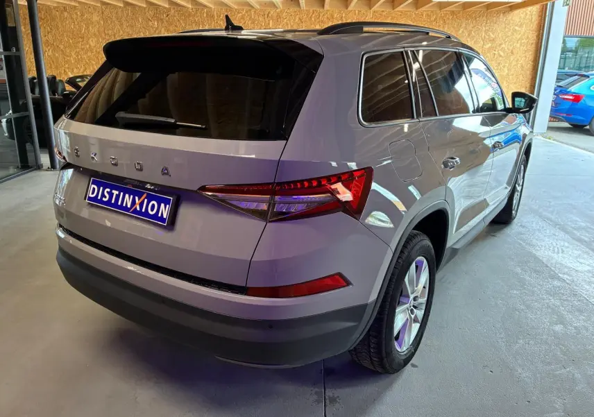 Vue 3/4 arrière droite d'un Skoda Kodiaq gris clair 2023 stationné en intérieur, avec vitres teintées et jantes alliage.