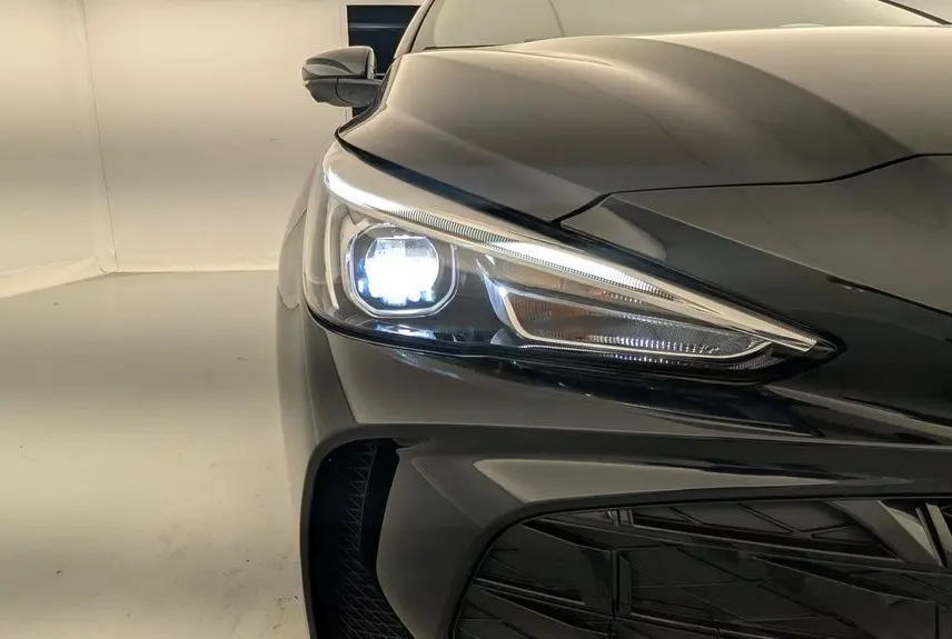 Gros plan sur le phare avant gauche allumé du MG3 Pebble Black 2026, mettant en valeur la calandre et la peinture métallisée.