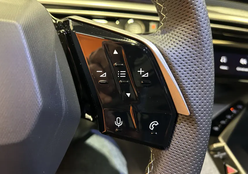 Gros plan sur les commandes tactiles noires du volant perforé côté gauche du Peugeot 3008 blanc Okenite, version hybride.