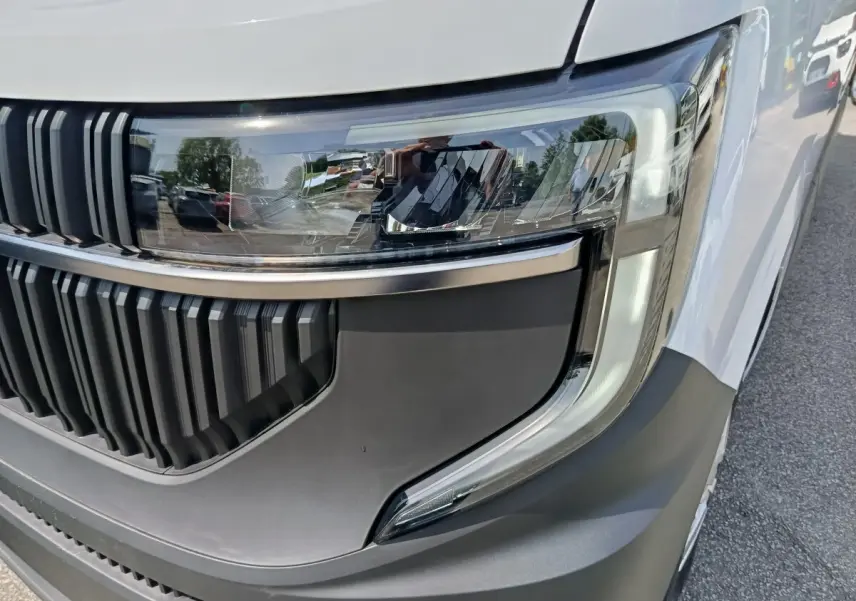 Gros plan sur le phare avant droit et la calandre noire du Renault Master blanc, avec détails LED et pare-chocs gris.