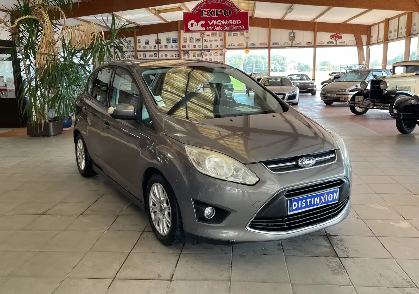 Ford C-MAX gris vue 3/4 avant droit dans un showroom avec plaque Distinxion visible sur le pare-chocs.
