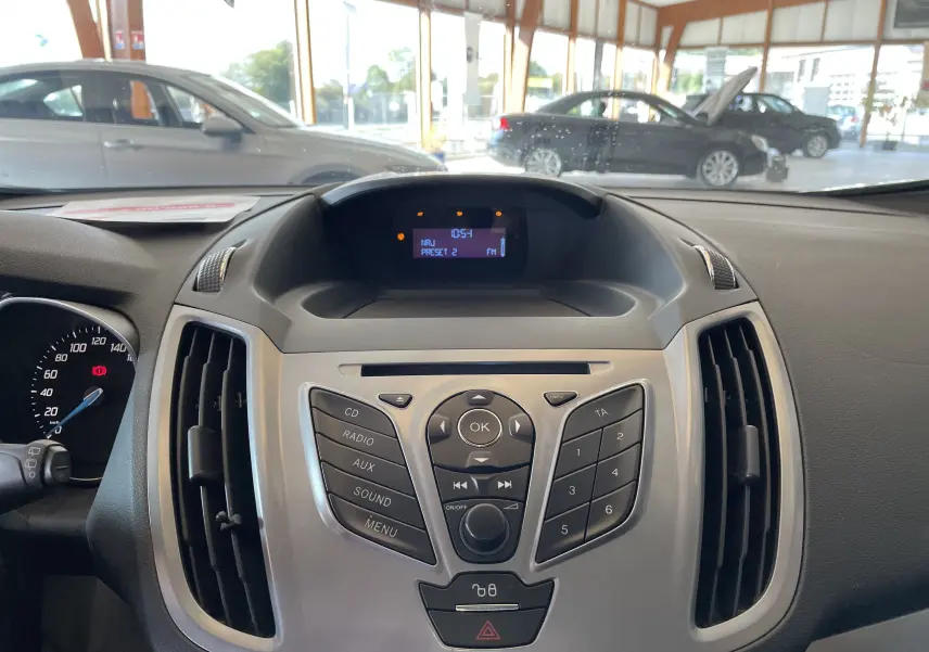 Tableau de bord central du Ford C-MAX gris 2012 avec commandes audio et écran digital affichant la radio FM.