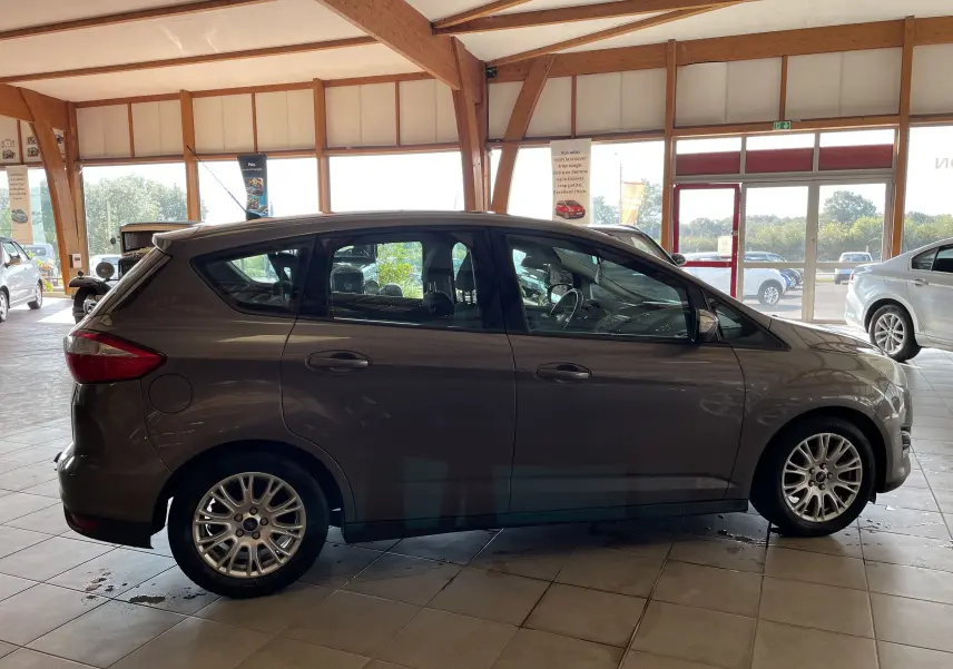 Ford C-MAX gris vue de profil côté gauche dans un showroom, soulignant ses jantes alliage et lignes compactes.