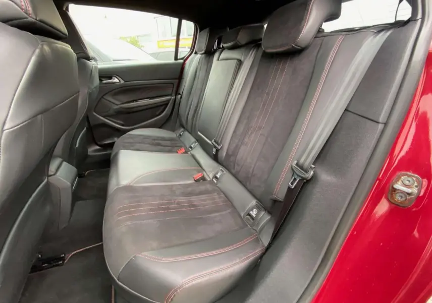 Vue intérieure côté arrière droit de la banquette en cuir noir avec surpiqûres rouges d'une Peugeot 308 GTi rouge.