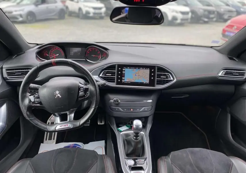 Vue intérieure avant du tableau de bord et volant GTi de la Peugeot 308 rouge, avec écran de navigation et boîte manuelle.