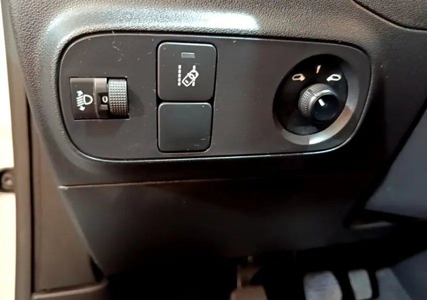 Gros plan sur les commandes de réglage des phares et des rétroviseurs côté conducteur d'une Citroën C3 blanche 2018.