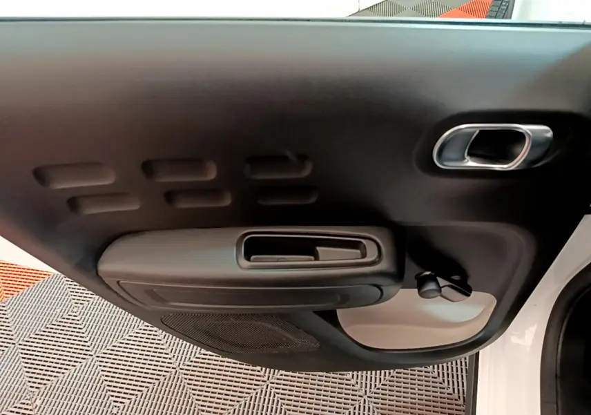 Vue rapprochée de la porte avant droite d'une Citroën C3 blanche, montrant la poignée intérieure et les commandes manuelles des vitres.