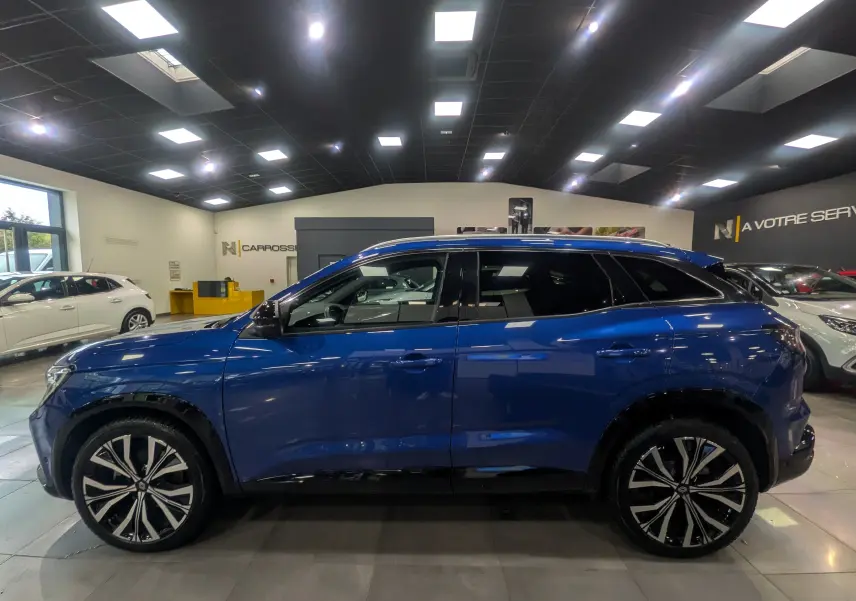 Profil latéral droit d'un Renault Austral E-Tech Hybrid 200 ch Iconic bleu Iron en showroom lumineux.