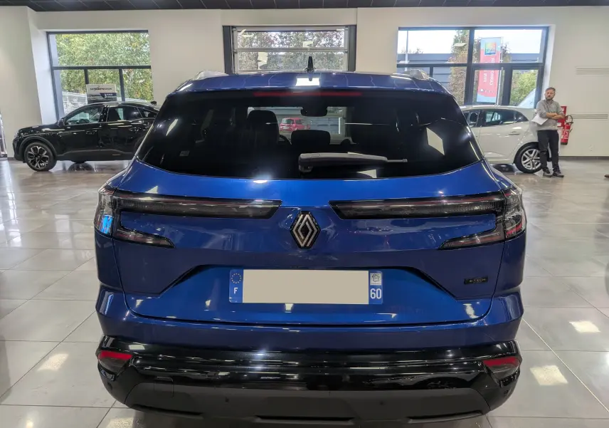 Vue arrière d'un Renault Austral E-Tech Hybrid bleu Iron en showroom, avec feux arrière LED et logo Renault central.