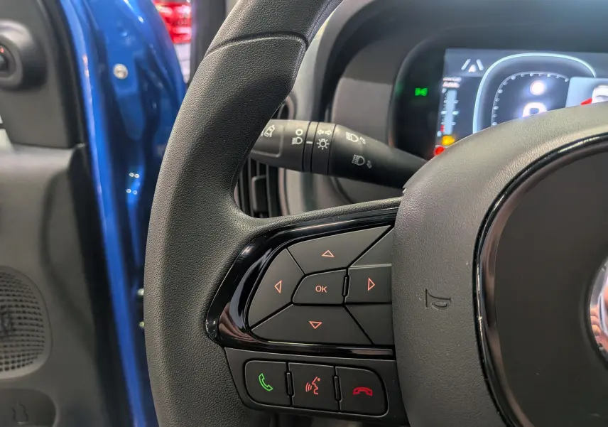 Gros plan sur le volant multifonction noir d'une Fiat Panda 1.0 Hybrid Bleu Italia avec portière côté gauche ouverte.