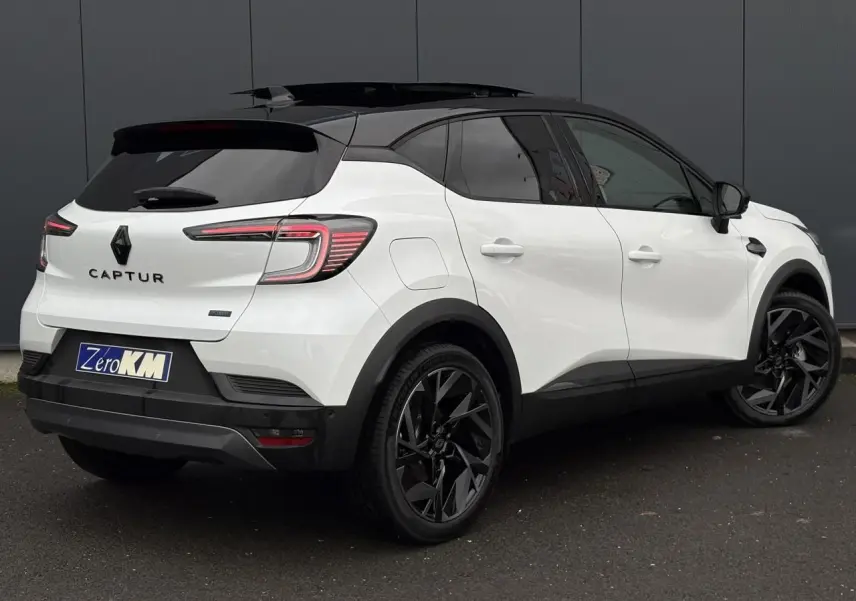 Vue 3/4 arrière droite du Renault Captur blanc nacré avec toit noir et jantes noires distinctives.