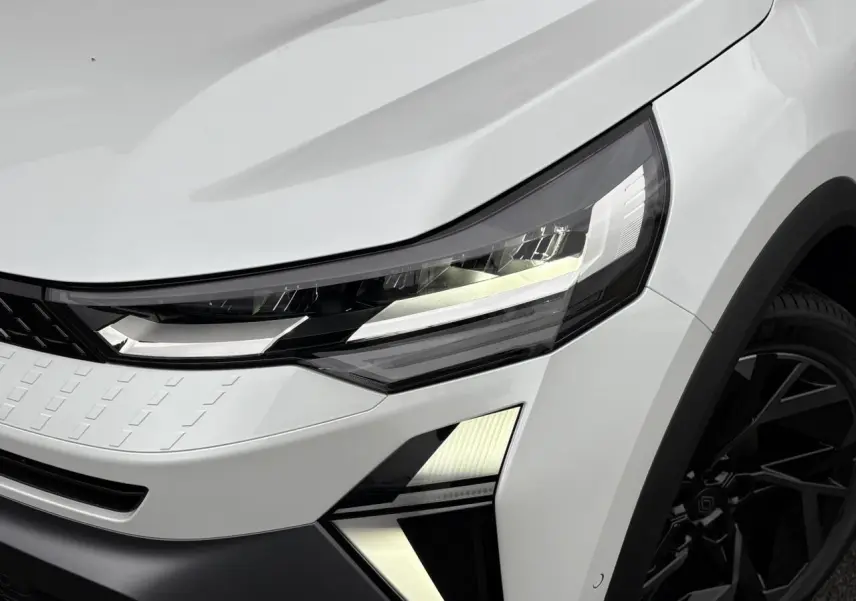 Gros plan sur l'avant droit du Renault Captur blanc nacré, mettant en valeur le phare LED et la jante noire design.