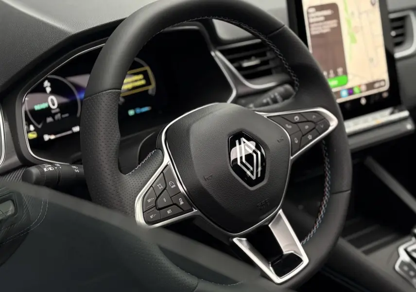 Gros plan sur le volant noir avec surpiqûres tricolores du Renault Captur 2025, tableau de bord numérique et écran tactile visibles.