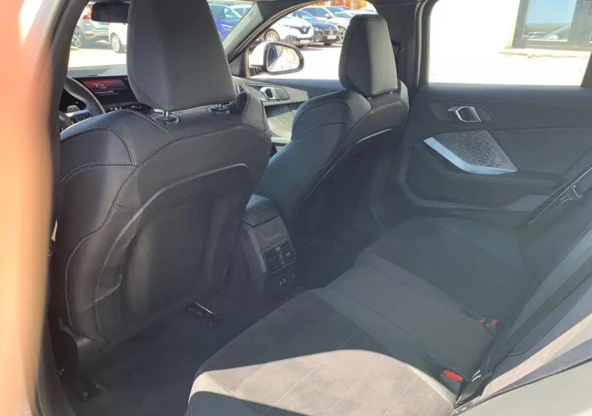 Vue intérieure arrière côté droit de la BMW Série 1 118D M Sport blanche avec sellerie Alcantara noire et surpiqûres bleues.