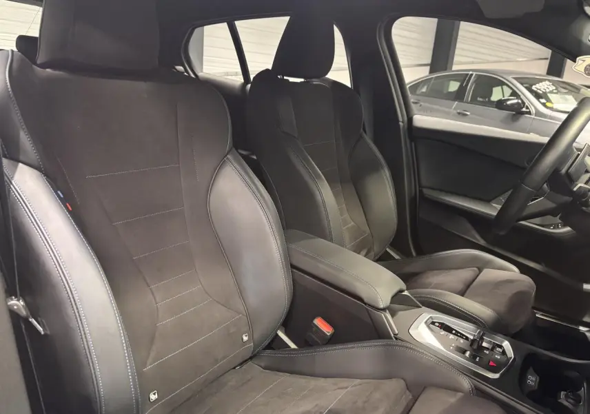 Vue intérieure sur les sièges avant sport en Alcantara noir avec surpiqûres bleues et console centrale de la BMW Série 1.