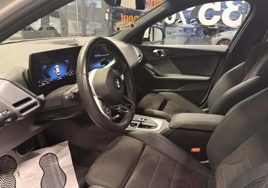 Intérieur BMW Série 1 118D 2025 vu côté conducteur, sièges sport Alcantara noirs et tableau de bord digital.