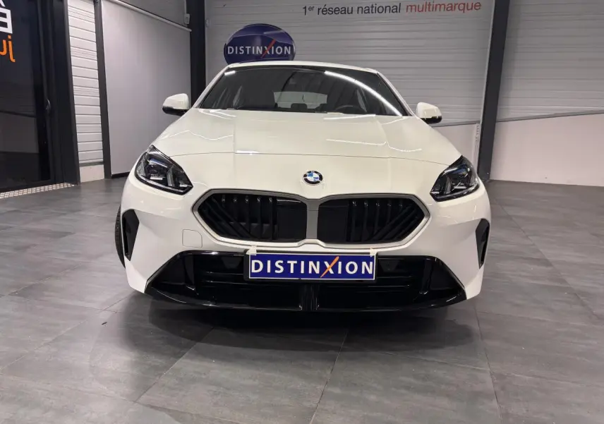 Vue avant d'une BMW Série 1 118D blanche avec calandre noire et projecteurs LED dans un showroom.