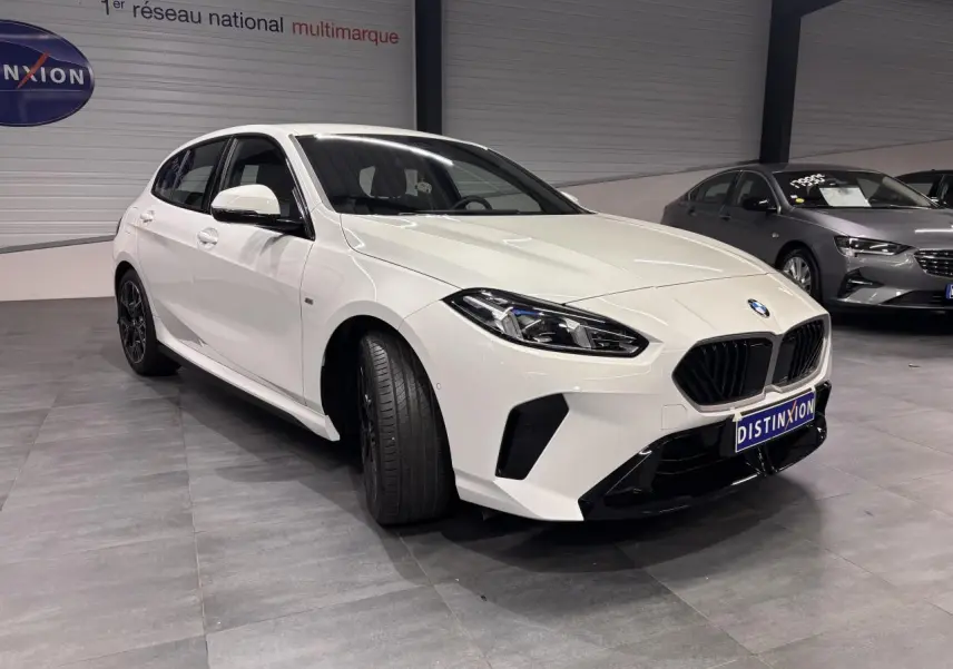 BMW Série 1 118D M Sport blanche vue 3/4 avant gauche avec calandre noire et jantes 18 pouces bicolores.