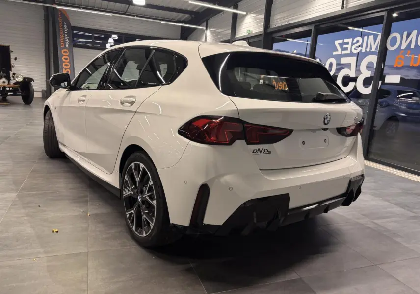 Vue 3/4 arrière droite d'une BMW Série 1 118D blanche en finition M Sport avec jantes 18 pouces en alliage bicolore.