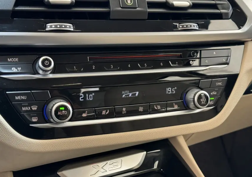 Gros plan sur la console centrale beige et noire du BMW X3 2018, avec commandes climatisation digitale et logo X3 visible.