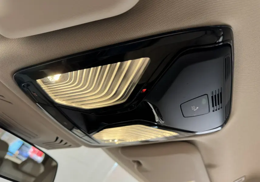 Plafonnier intérieur noir brillant avec éclairage LED et bouton SOS dans un BMW X3 gris foncé, vue en contre-plongée.