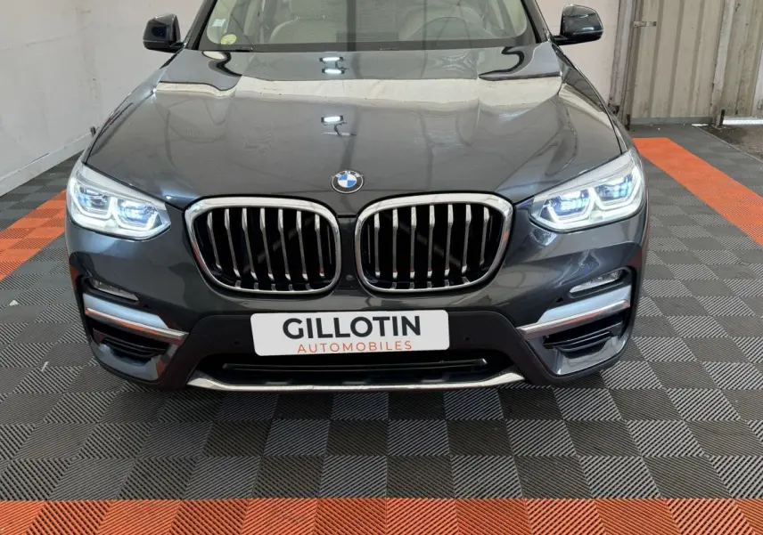 Vue frontale d'une BMW X3 xDrive30d gris foncé avec phares LED allumés et calandre double haricot chromée.