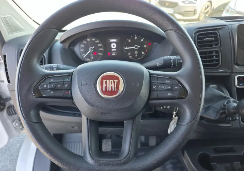 Vue intérieure centrée sur le volant noir du Fiat Ducato Fourgon blanc avec tableau de bord et levier de vitesses manuel.