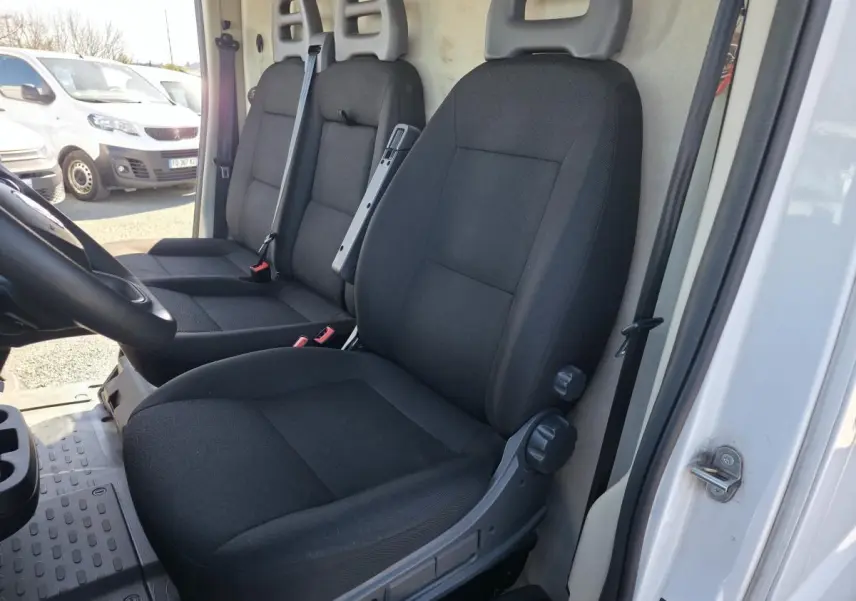 Vue intérieure côté conducteur du Fiat Ducato Fourgon blanc 2023, montrant les sièges noirs et la cloison tôlée arrière.