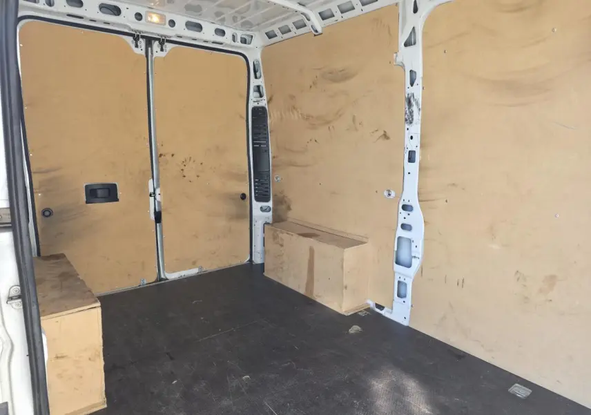 Intérieur du fourgon FIAT Ducato Maxi blanc vu de l'arrière, montrant la cloison tôlée et le revêtement bois des parois.