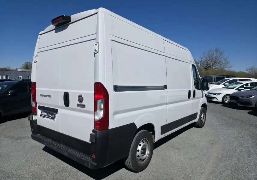 Vue 3/4 arrière droite d'un FIAT Ducato Fourgon blanc tôlé Maxi avec porte latérale coulissante, sur parking extérieur.
