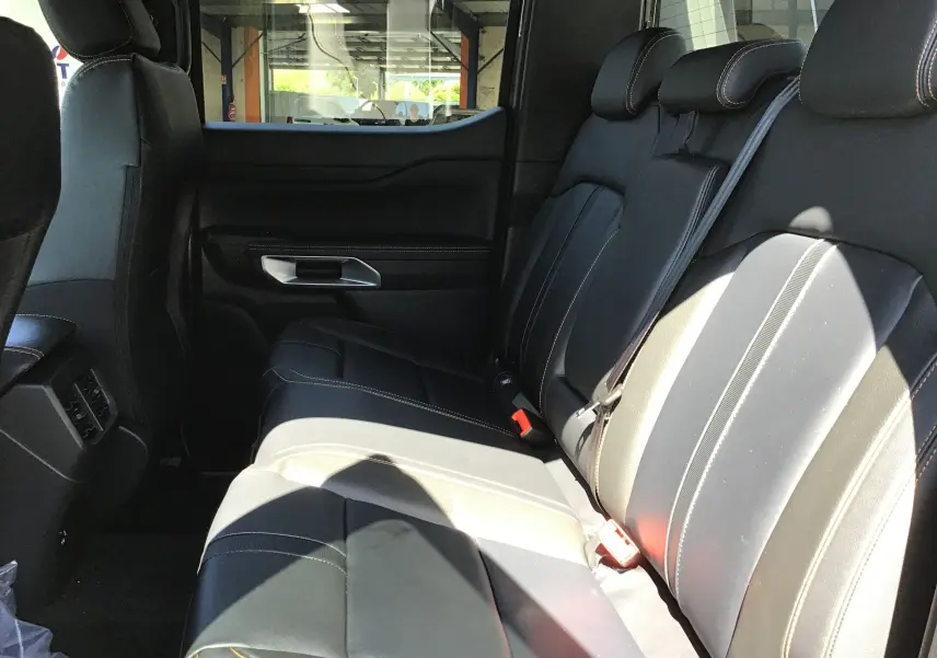 Vue latérale des sièges arrière en cuir noir avec surpiqûres orange du Ford Ranger Double Cabine gris carbone 2025.