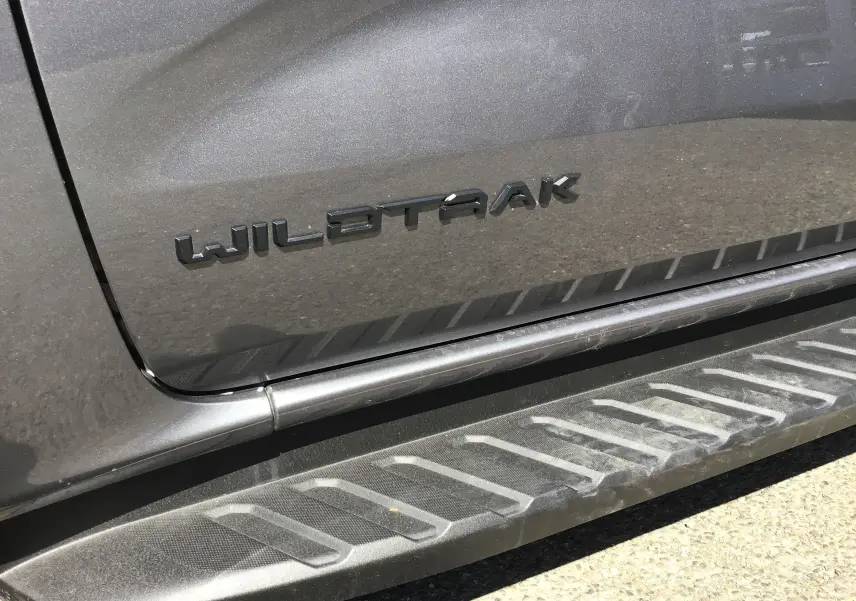 Gros plan sur la porte côté gauche gris carbone d'un Ford Ranger Wildtrak avec logo et marchepied texturé.