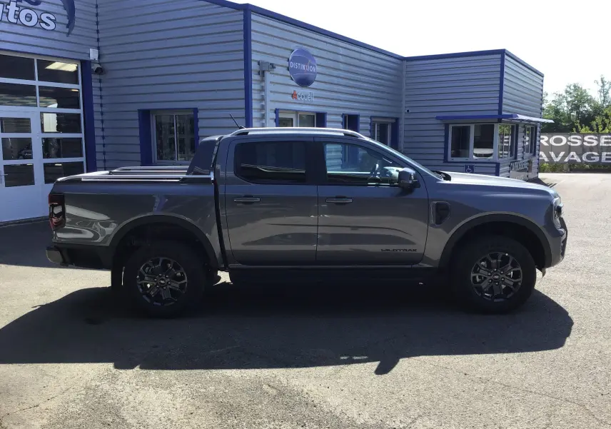 Ford Ranger Double Cabine Wildtrak gris carbone vu de profil côté gauche avec rideau de plateau coulissant et marchepied visible.