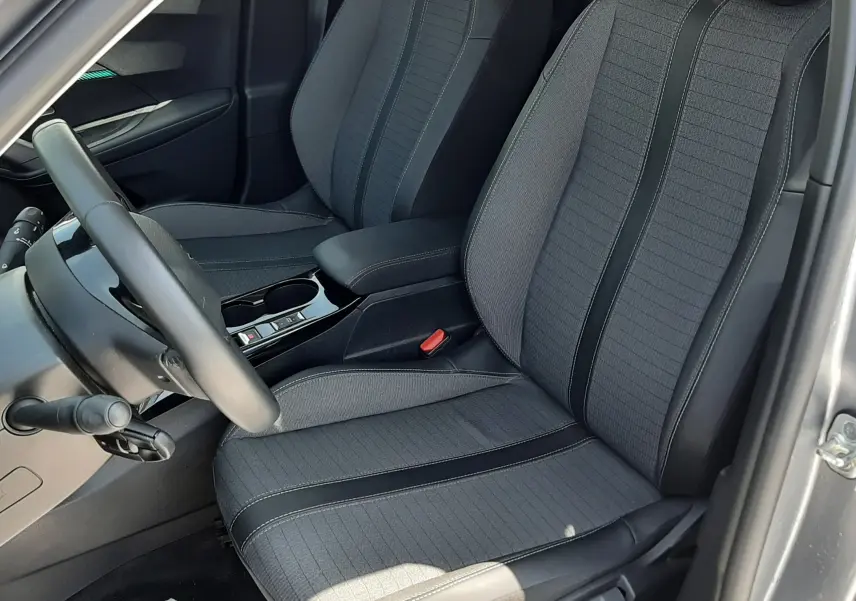 Vue intérieure côté conducteur du Peugeot 2008 gris Artense, mettant en valeur les sièges tissu et cuir noir avec coutures contrastées.