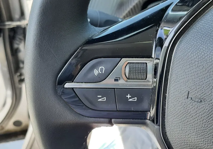 Gros plan sur les commandes du volant à gauche du Peugeot 2008 gris Artense, avec boutons de volume et commande vocale.