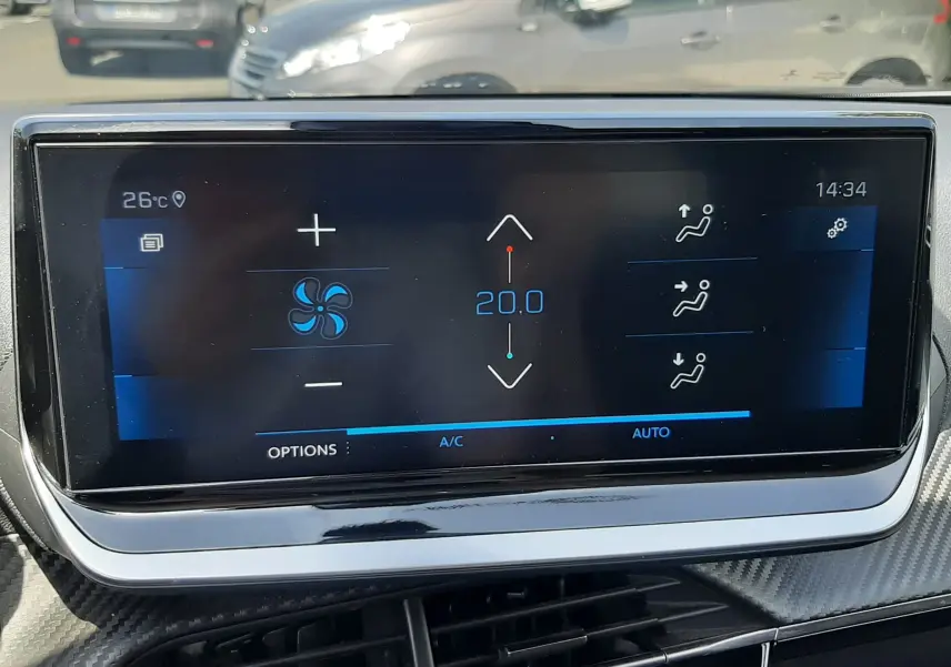 Écran tactile de climatisation affichant 20°C dans l'habitacle d'un Peugeot 2008 gris Artense visible en arrière-plan.
