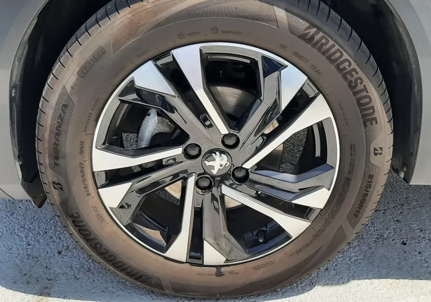 Gros plan sur la roue avant gauche d'un Peugeot 2008 gris Artense avec jante alliage bicolore et pneu Bridgestone.