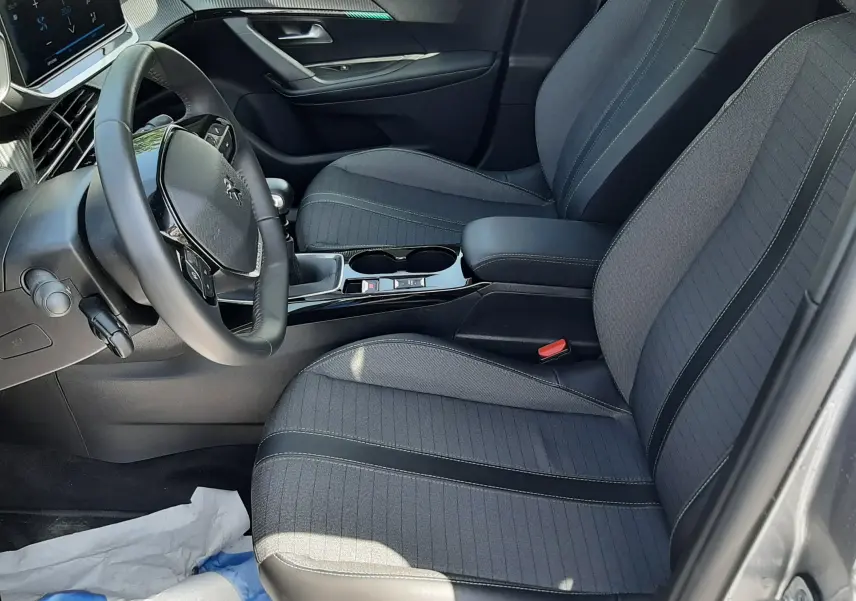 Intérieur avant droit du Peugeot 2008 2022 gris Artense, sièges tissu noir avec coutures contrastées et tableau de bord moderne.