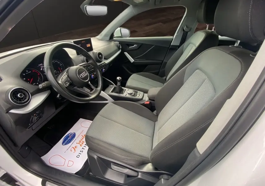 Vue intérieure côté conducteur de l'Audi Q2 30 TDI 2019 avec sièges tissu gris et volant multifonction noir.