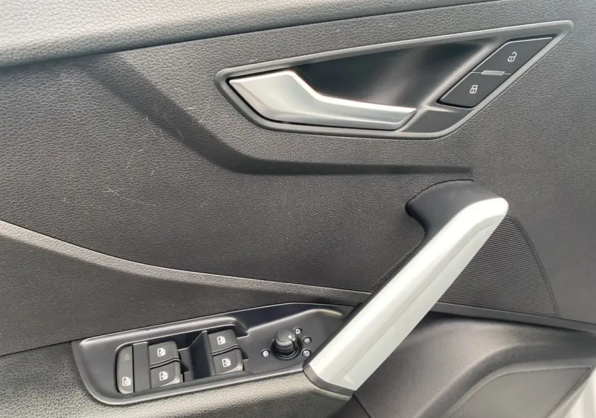 Poignée de porte intérieure côté gauche de l'Audi Q2 blanc, avec commandes de vitres et verrouillage intégrées.