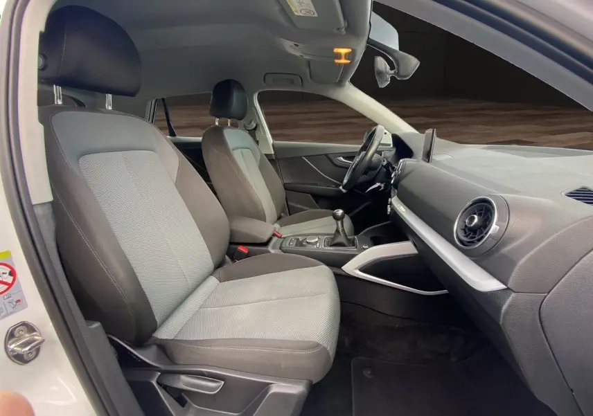 Vue intérieure côté conducteur de l'Audi Q2 30 TDI 2019 avec sièges tissu gris et tableau de bord noir.