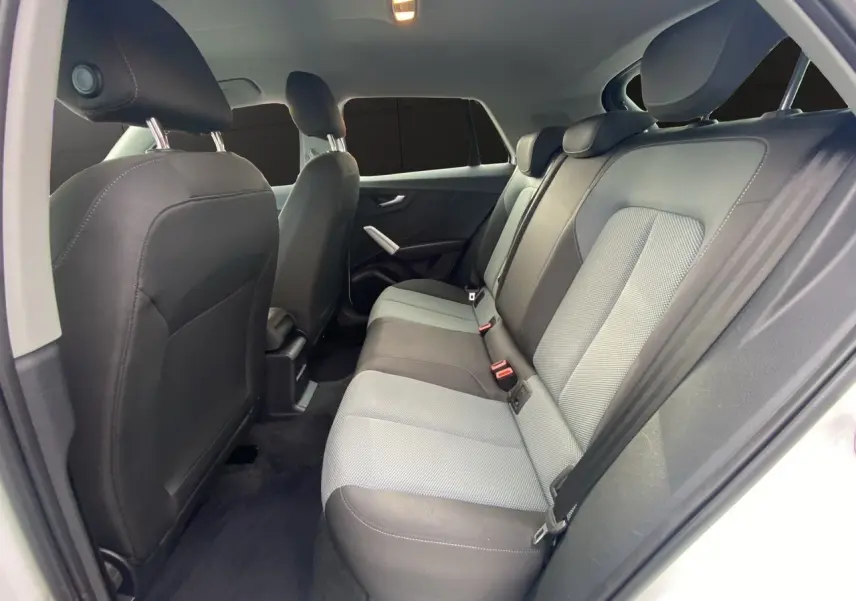 Vue intérieure arrière de l'Audi Q2 30 TDI blanc, sièges tissu noir et gris avec appuie-têtes et ceintures visibles.