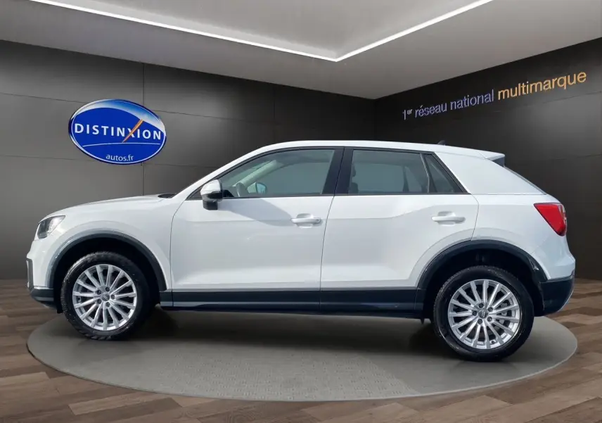 Audi Q2 blanc en profil côté gauche, SUV compact avec jantes alliage et lignes épurées en showroom.