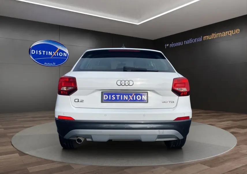 Vue arrière d'un Audi Q2 blanc 30 TDI 2019 avec feux rouges et logo distinctif sur fond sombre intérieur showroom.