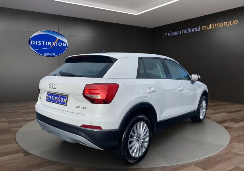 Audi Q2 blanc vue 3/4 arrière droit, avec jantes alliage et feux arrière LED dans un showroom.