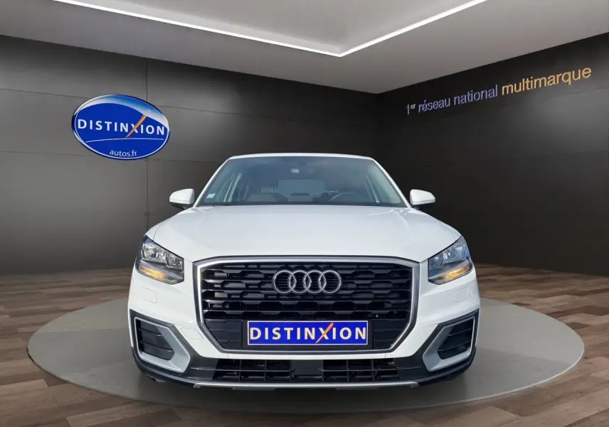 Audi Q2 blanc vue de face mettant en valeur sa calandre noire et ses phares LED allumés dans un showroom.